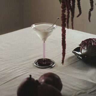 Martini glass with a pink cocktail on a table with pears and a plant in the background