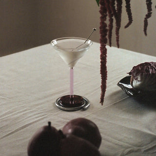 Martini glass with a pink cocktail on a table with pears and a plant in the background